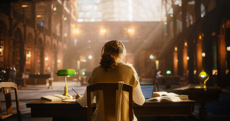 Serene Female Student Engaged in Online Learning in a Classical Library. Young Woman Wearing Headphones, Using Laptop and Books to Study Amidst Classical Architecture and Wooden Furniture.