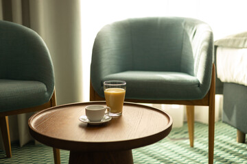 Interior of living room with coffee table with fresh juice. Fresh blended peach smoothie and cup of coffee on wooden table, morning in hotel