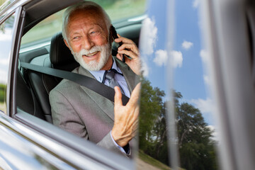 Elegant senior businessman chatting on phone while riding in a luxury car