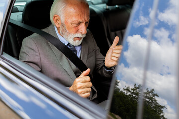 Senior businessman working on laptop while riding in backseat of car