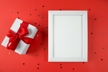 Top view photo of gift box and white wooden frame with empty space on red background.
