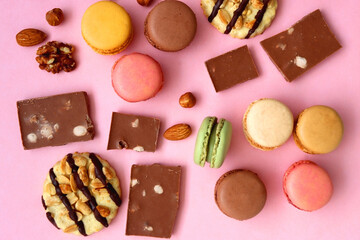 Pastel macarons, almond chocolate, peanut butter cookies and various nuts on bright pink background. Top view.