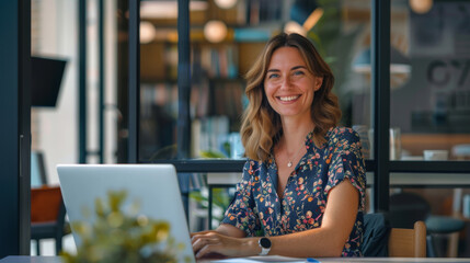 A woman with a happy expression sitting at a desk working on a laptop computer