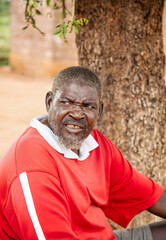 old african man in the village siting in the yard, under a tree in the shade