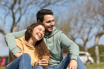 couple enjoying outdoors in a park while enjoying and having fun and drinking coffee in a reusable cup