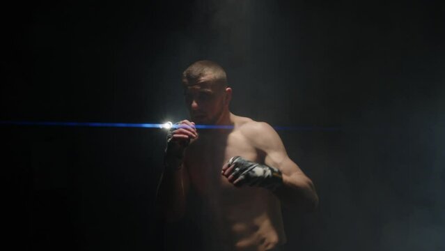 mixed martial arts fighter with bandaged fists punches the camera. a boxer beats an imaginary opponent. backlight anamorphic cinematic effect