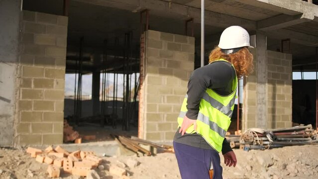 Worker man limps on construction site in back pain. Body damage while working. Prevention and safety first.