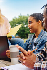 latina girl using laptop while working on a class project with her classmates sitting on a bench on...