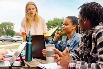 multiracial group of young students sitting together on a university campus bench with academic...