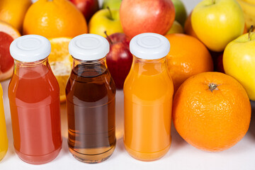 Assortment of fruit juices in glass bottles among fruits on white background