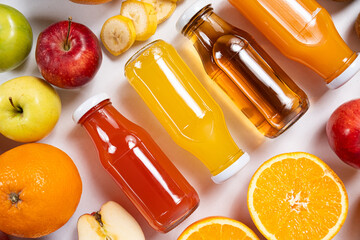 Assortment of fruit juices in glass bottles among fruits on white background top view