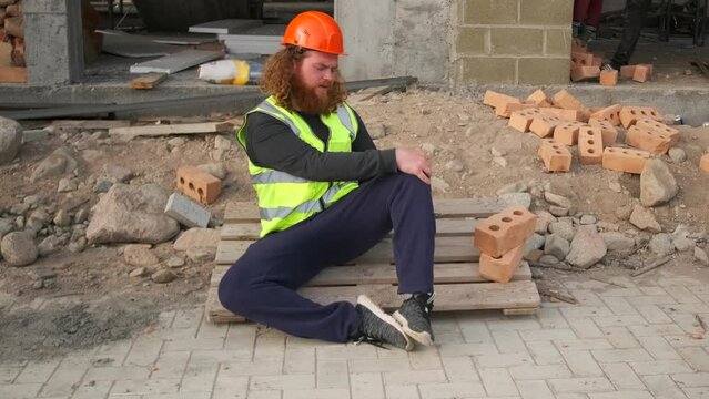Worker suffering from leg pain resulting from an injury on a construction site calls an employee to call an ambulance. Slow motion.
