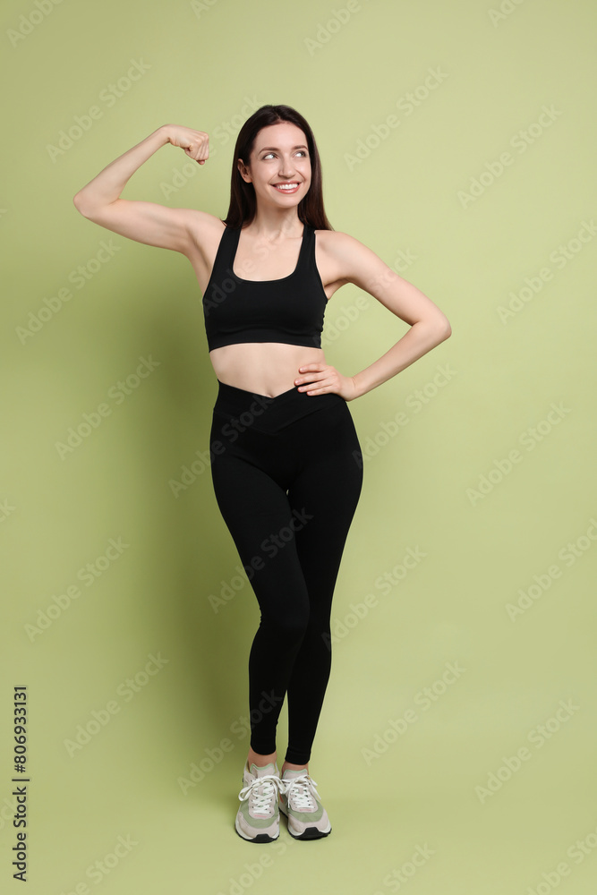 Wall mural Happy young woman with slim body showing her muscles on green background