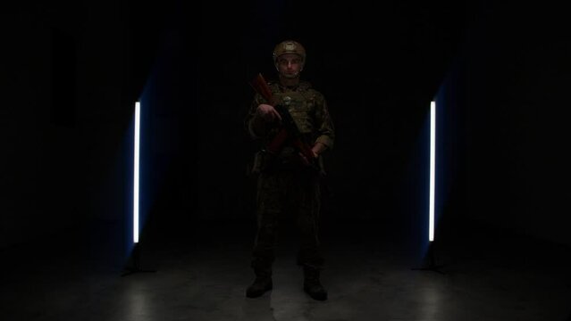 military man in ammunition with a weapon in his hands in a dark room on the background of a black wall. general plan a special officer