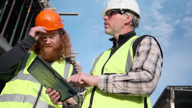 Construction worker specialist discussing project work with man engineer contractor holding tablet computer at construction site.