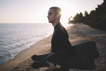Portrait of young active man wearing wetsuit and holding diving fins ready to dive into water