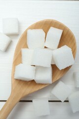 Many sugar cubes and wooden spoon on white table, top view