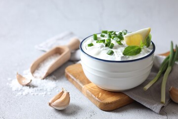 Delicious yogurt with green onion in bowl, garlic, salt and lemon on light textured table, closeup