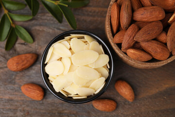 Fresh almond flakes in bowl and nuts on wooden table, flat lay