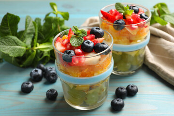 Delicious fruit salad in glasses, fresh berries and mint on light blue wooden table