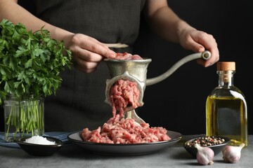 Woman making beef mince with manual meat grinder at grey table, closeup