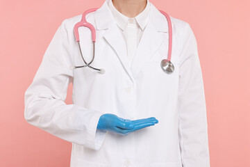 Doctor with stethoscope holding something on pink background, closeup