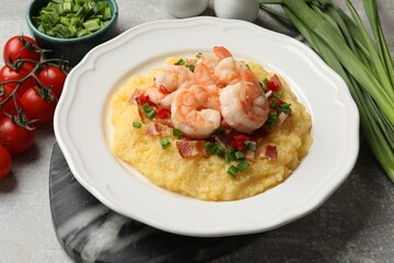 Plate with fresh tasty shrimps, bacon, grits, green onion and pepper on gray textured table, closeup