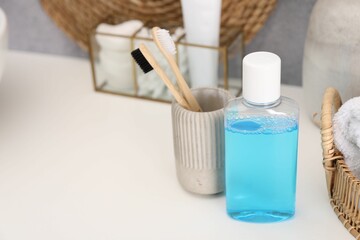 Bottle of mouthwash and toothbrushes on white table in bathroom, space for text