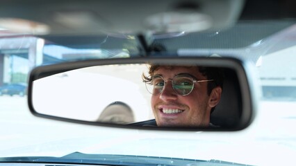 Happy young man in stylish glasses driving car and looking at rear view mirror. Transport and lifestyle concept. Real time