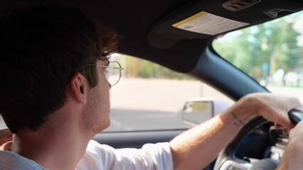 Smiling young man driving his car, turning the steering wheel and carefully looking at the road. Side view. Transport and lifestyle concept. Real time