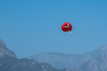 Person goes parasailing. Red parachute against the background of mountains and blue sky.