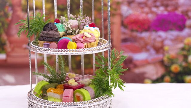 Afternoon Tea or High Tea Display in the silver rack with flowers, macaron, scone, cake, cup cakes, on colorful background
