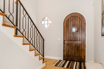 an entry way with white walls and a wooden door with a black iron railing,