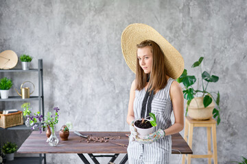 Portrait of Woman gardener transplanting plants. Concept of home garden. Flower and garden shop. A straw hat with a wide brim.