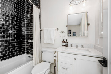 a bathroom with white cabinets, toilet and bathtub with black tiles on the walls