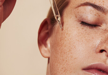 Close-up highly detailed shot of female skin with freckles and pipette with serum. Cropped shot of...