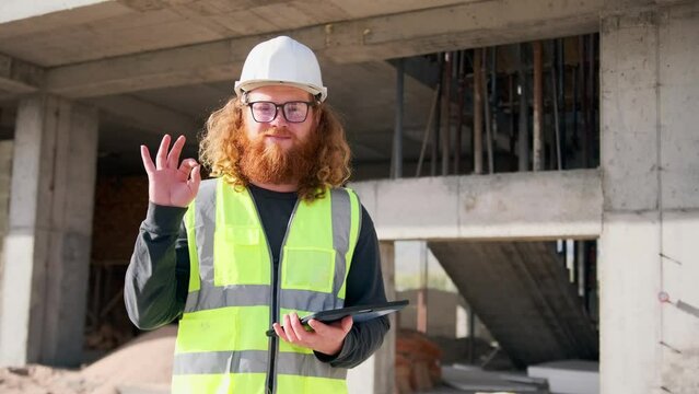 Positive man architect showing hand with OK sign,  good job on construction site,  quality control and building inspection, bearded redhead guy millennial construction worker.