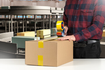 Man packs boxes. Guy seals package with tape. Cropped packer at work. Tape dispenser in hands of storekeeper. Man packer near conveyor. Fulfillment center employee. Logistics hub packer
