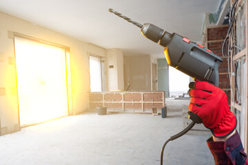 Electric drill in hand of builder. Equipment for drilling holes. Drill for repair work. Hand of builder in room being repaired. Electric hammer drill from master. Provision of repair services concept