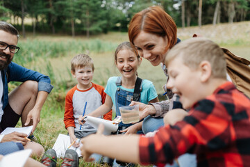 Young students analyzing water quality, ph level with indicator strips during biology field teaching class. Female teacher during outdoor active education.