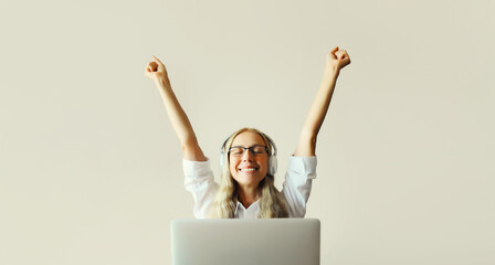 Happy joyful woman listening to music in headphones working with laptop sitting at desk at home