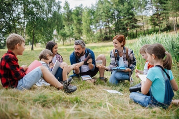 Fototapeta premium Young students analyzing water quality, ph level with indicator strips during biology field teaching class. Female teacher during outdoor active education.