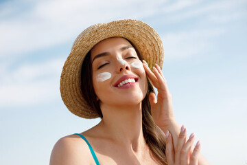 Beautiful young woman at beach applying sunscreen on face and looking at camera. Beauty girl...
