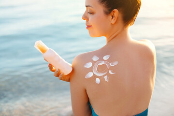 Woman Applying Sun Cream on Tanned Shoulder In Form Of The Sun. Sun Protection.Sun Cream. Skin and Body Care. Girl Using Sunscreen to Skin. Female Holding Suntan Lotion and Moisturizing Sunblock