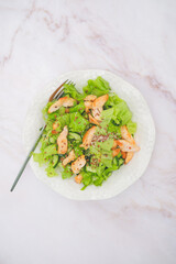 Plate with healty salat - chicken, cucumber, lettuce leaves, flax seeds on white marble background. Top view.