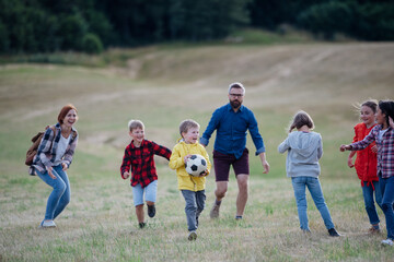Young students playing with teacher outdoors, in nature, during field teaching class, running with ball. Dedicated teachers during outdoor active education.