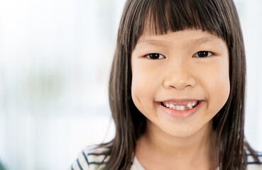 Close up portrait of young fun smart happy little cute asian girl with milk teeth studio shot....