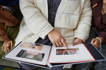 Close up of senior woman with two children looking at pictures in photo album and sharing family...