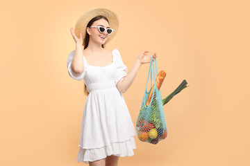 Woman with string bag of fresh vegetables and baguette on beige background