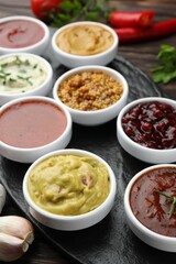 Different tasty sauces in bowls and garlic on table, closeup